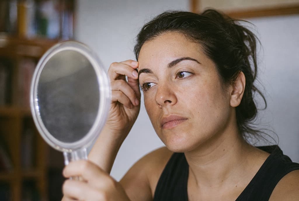 Persona observando con calma sus cejas frente a un espejo