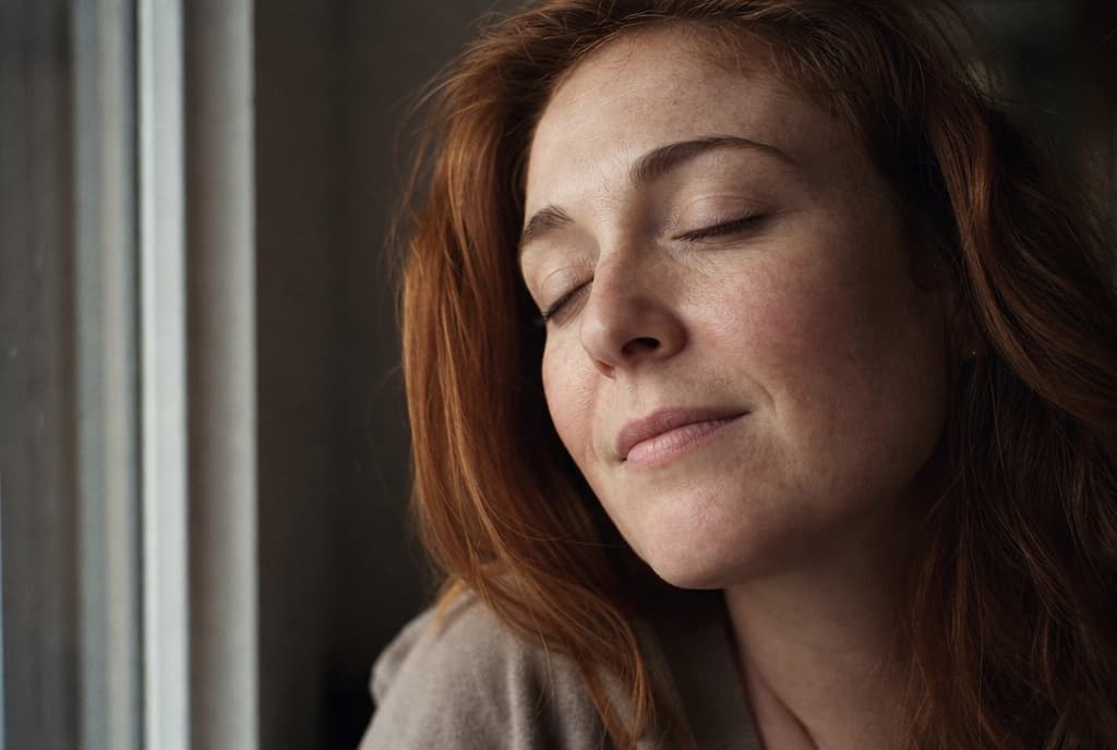 Rostro relajado de una mujer junto a una ventana, ojos suavemente cerrados